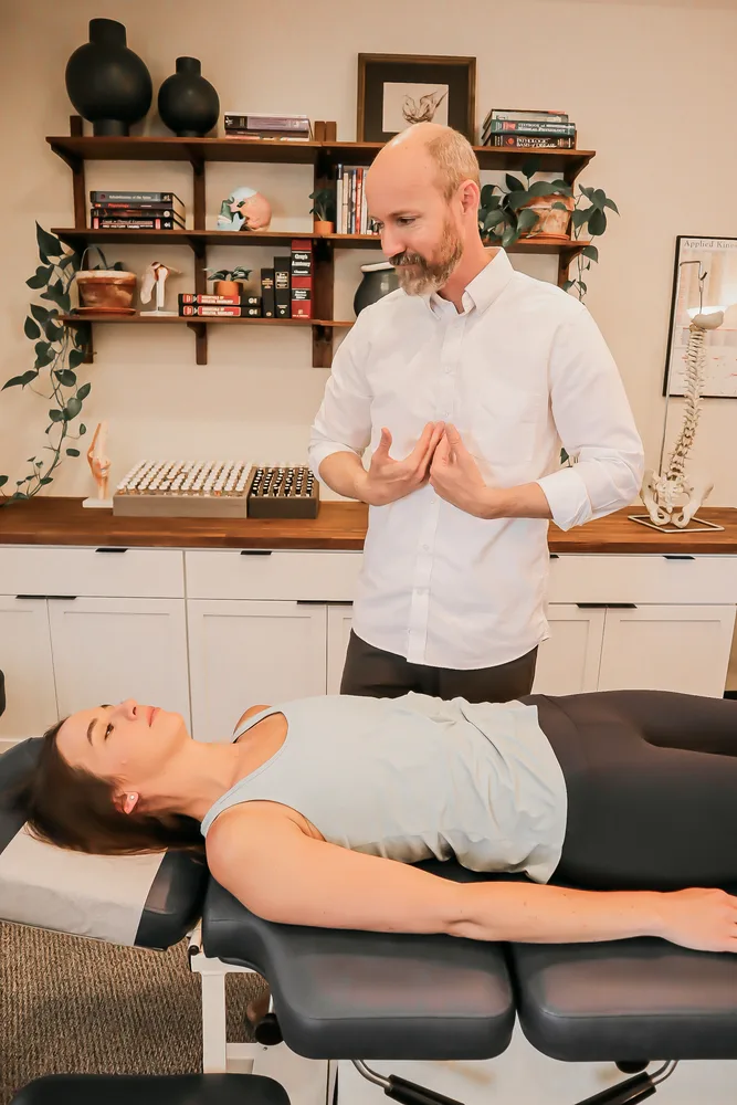 Dr. Andrew Rostenberg performing applied kinesiology testing with nutrient and remedy vials over a patient on the adjusting table at Red Mountain Natural Medicine in Boise, Idaho — used alongside genetic and methylation lab data to refine treatment